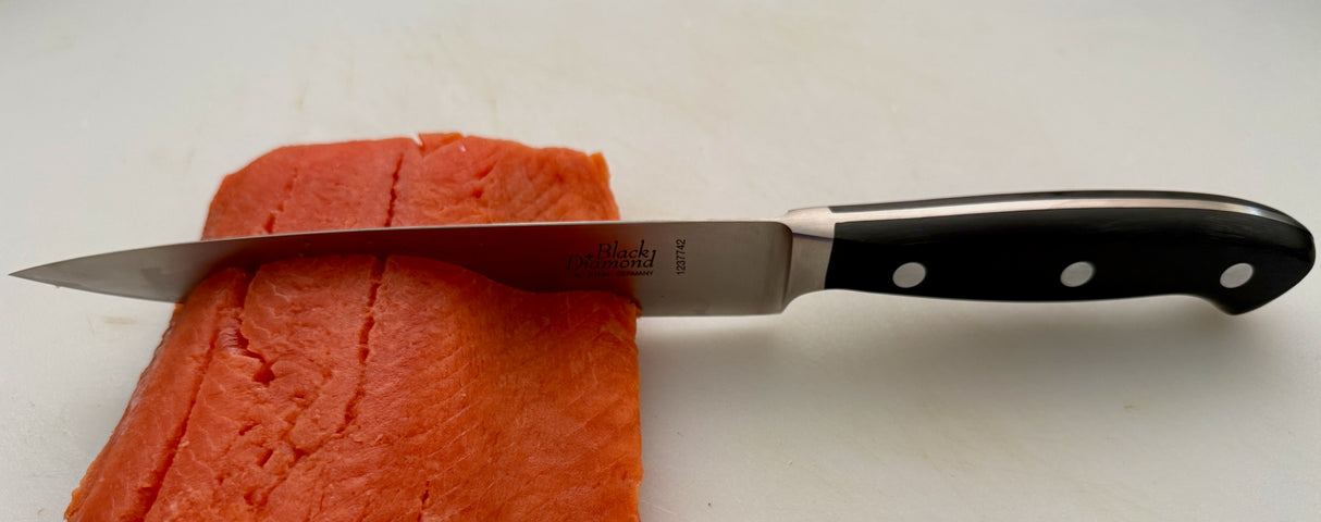 Filleting knife cutting salmon; stainless blade and black handle with white rivets