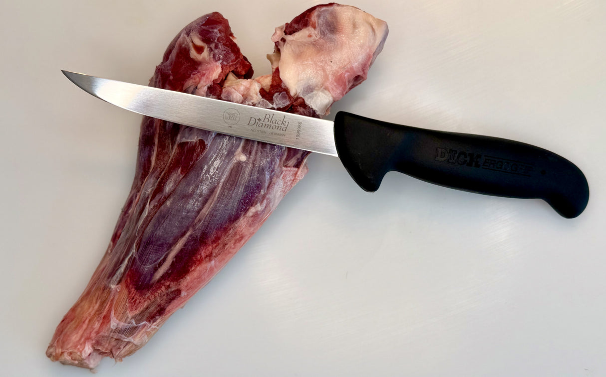 Boning knife with stainless blade and black handle next to raw meat and bone