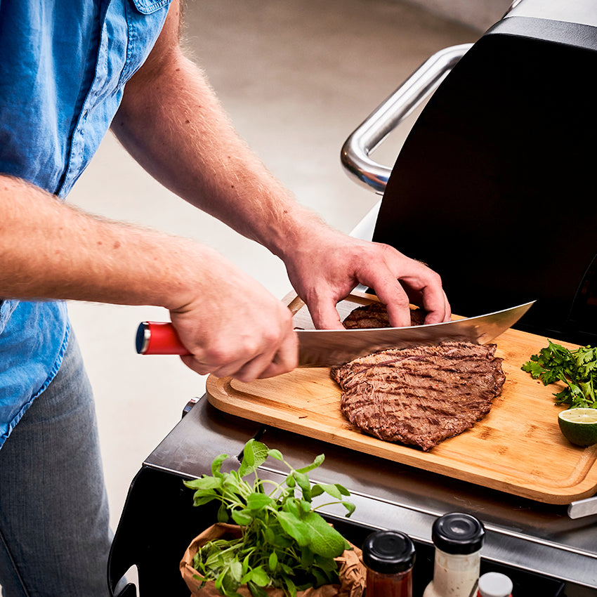 10-inch butcher knife with red handle, slicing meat on a wooden cutting board