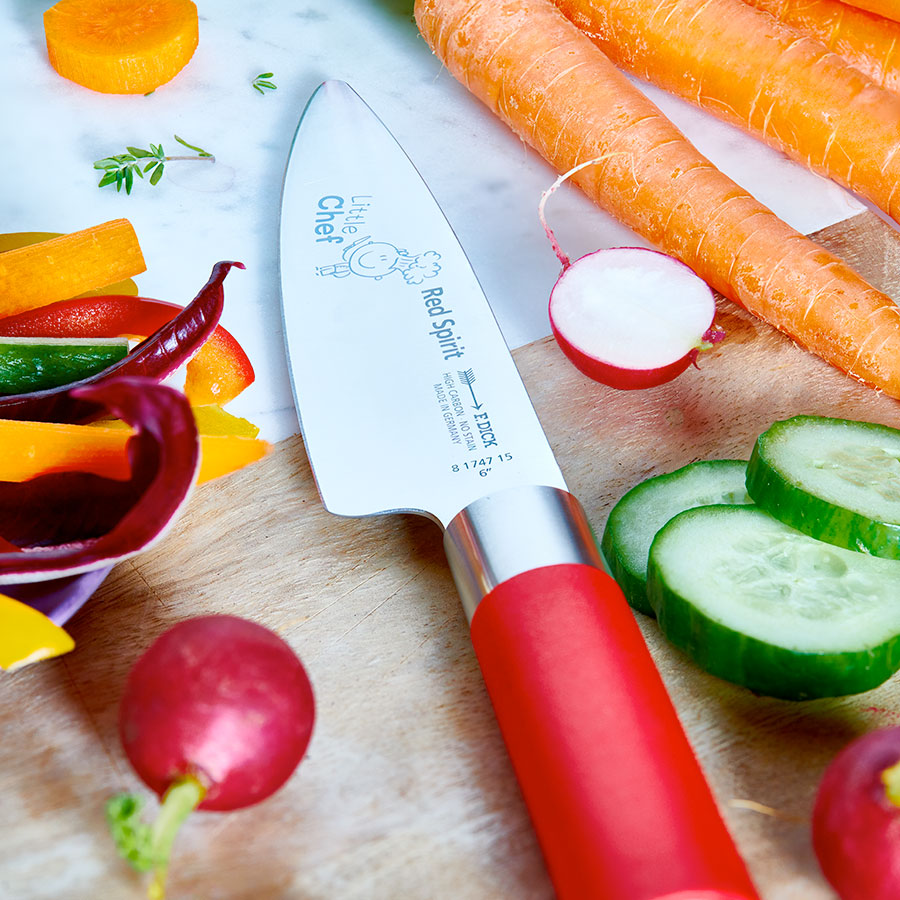 Chef's knife with red handle and printed blade on a cutting board with vegetables