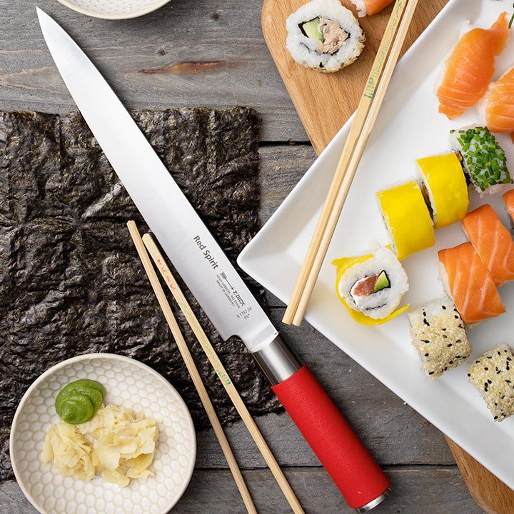 Sushi knife with long white blade and red handle, with chopsticks and sushi nearby