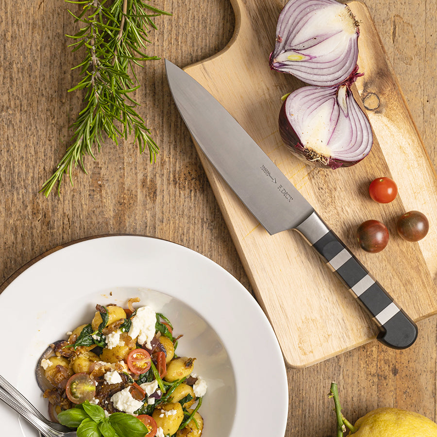 F.Dick chef knife with black handle and 6in stainless blade, angled on cutting board