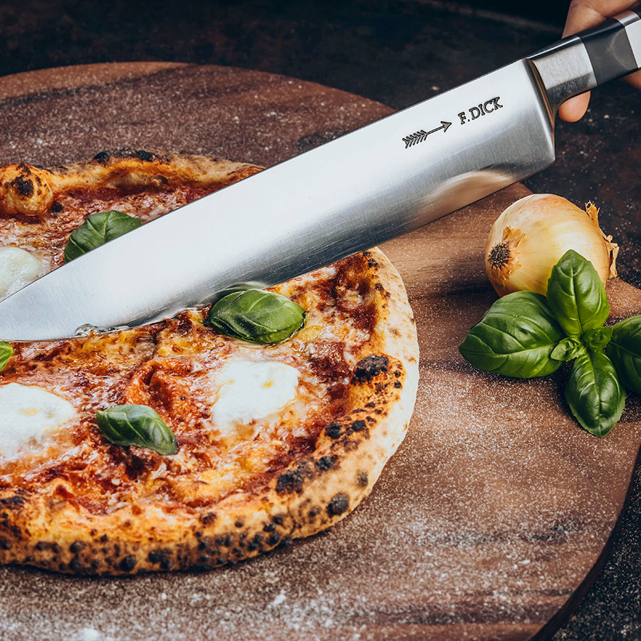 F.Dick chef knife with stainless blade and black handle, angled beside pizza.