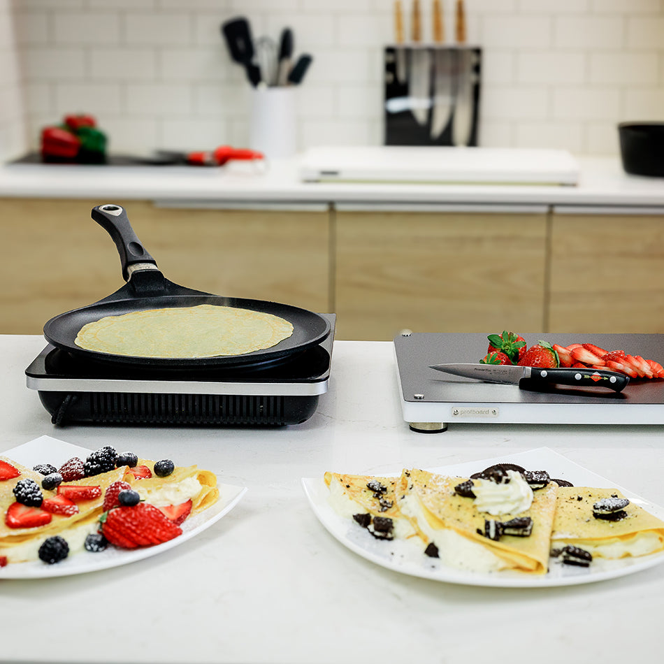 AMT crepes pan cooking a crepe, with fruit-topped crepes on nearby plates