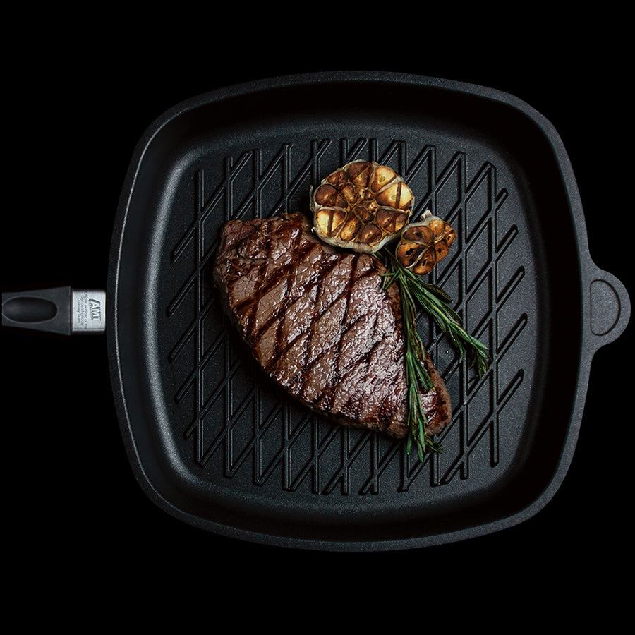 Square black grill pan with embossed ridges and side handles, steak with rosemary