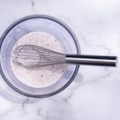 Stainless steel wire whisk stirring pale batter in bowl