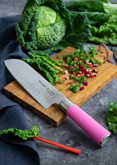 Pink-handled santoku knife with scalloped edge on a wooden cutting board