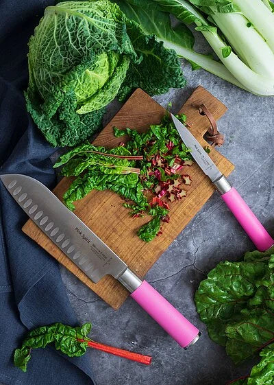 Pink-handled santoku knife cutting greens on a wooden board