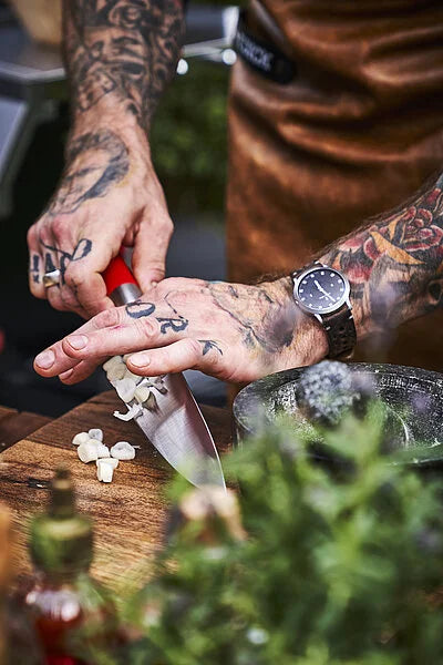 Chef knife with red handle in hands, stainless blade cutting on wooden board