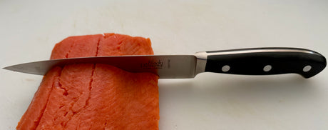 Filleting knife cutting salmon; stainless blade and black handle with white rivets