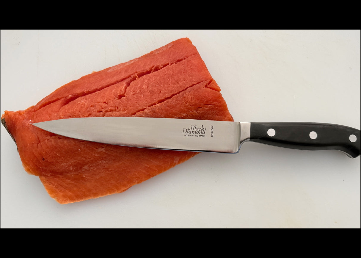 7-inch filleting knife with stainless blade and black handle, beside salmon fillets