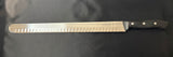 Serrated carving and slicing knife with steel blade and black handle, side view