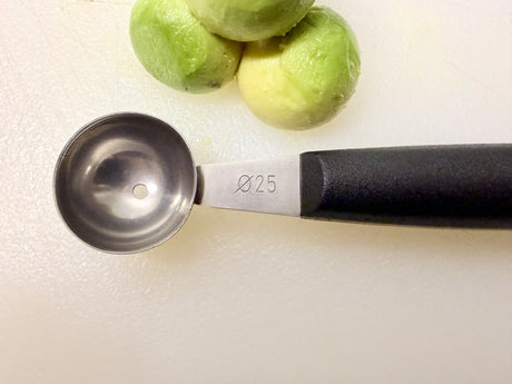 Melon baller with stainless steel scoop on black handle, shown with melon balls