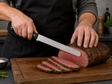 Roast beef slicer cutting thin slices from a roast on a wooden board