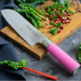 Pink-handled santoku knife on a wooden board with chopped greens in background