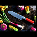 Red-handled Santoku knife on dark surface with vegetables