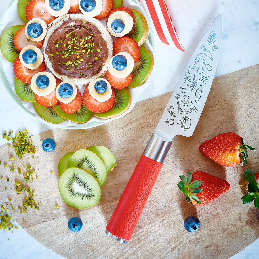 Red-handled chef's knife beside fruit tart, strawberries, and kiwi slices