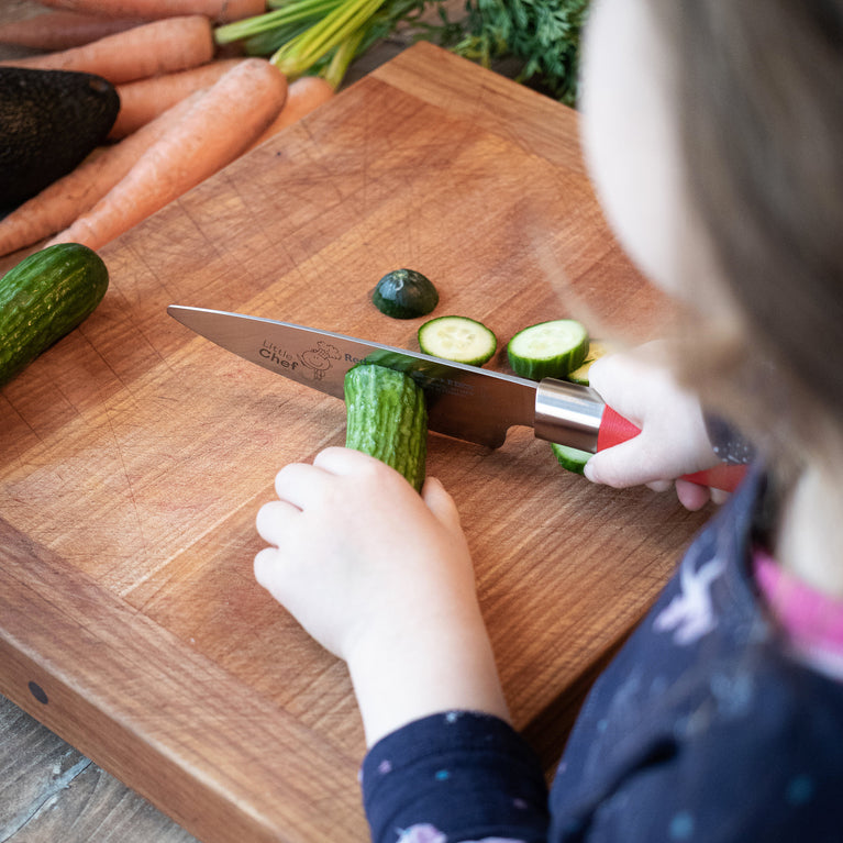 Red-handled chef's knife slicing cucumber on a wooden cutting board