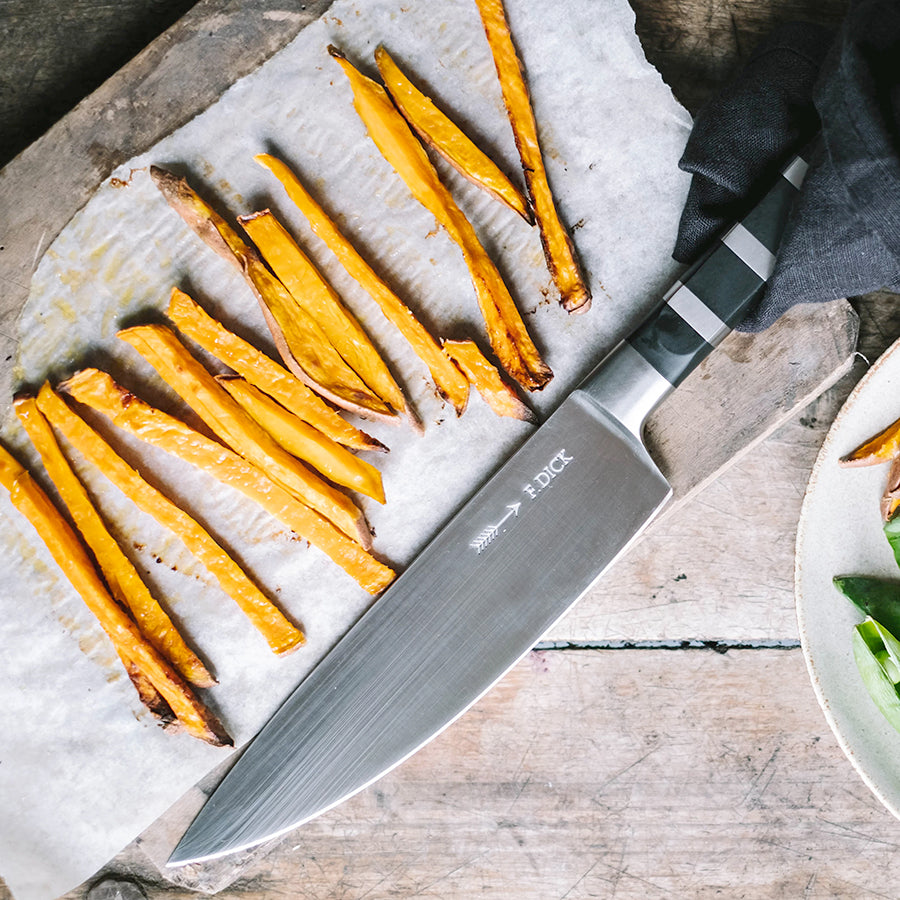 Chef knife with stainless blade and black handle beside sliced orange vegetables
