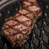 Square black grill pan with ridged grill surface and seared steak