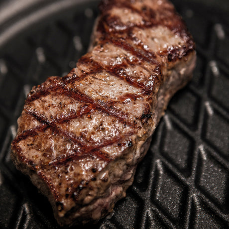 Square black grill pan with ridged grill surface and seared steak