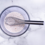Stainless steel wire whisk stirring pale batter in bowl