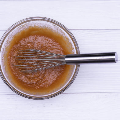Stainless steel wire whisk mixing amber batter in bowl