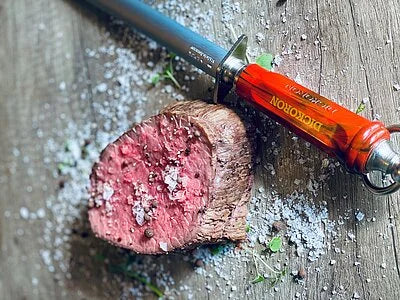 DICKORON knife with red-and-orange handle and silver blade slicing meat