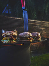 10-inch butcher knife with red handle held near grilled meat on a griddle