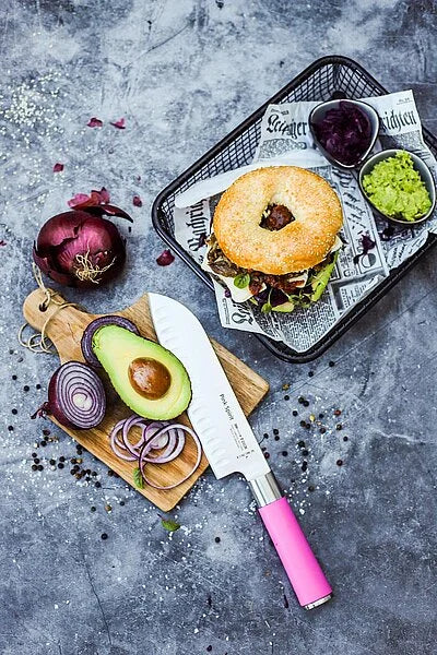 Pink-handled santoku knife on a cutting board with avocado and sliced onions