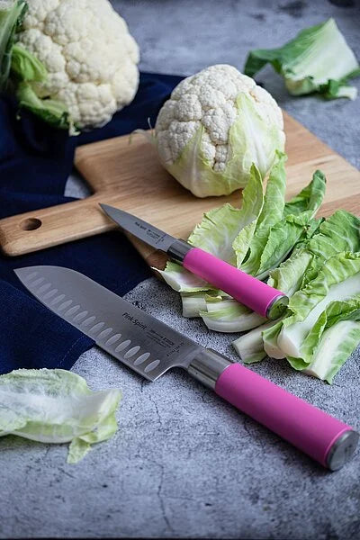 Pink-handled santoku knife beside cauliflower and lettuce on a wooden board