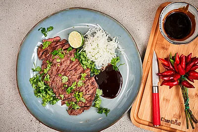 Red-handled paring knife with silver blade beside a plate of food on a board