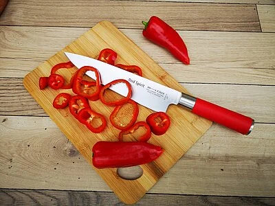 Chef knife with red handle and stainless blade on wooden cutting board