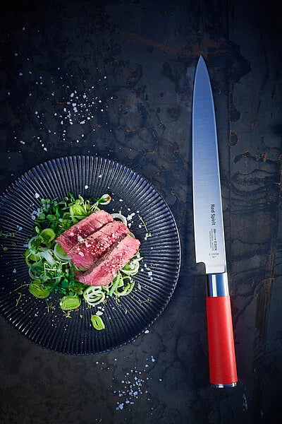 Sushi knife with long stainless blade and red handle on dark plate