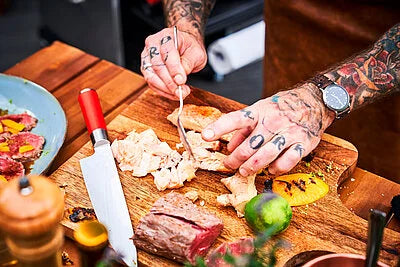 Chef knife with red handle and white blade cutting food on a wooden board