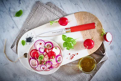 Chef knives with red handles beside sliced onions and herbs on a plate