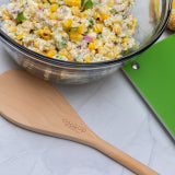 Wooden serving spoon with engraved logo, shown beside a bowl of food